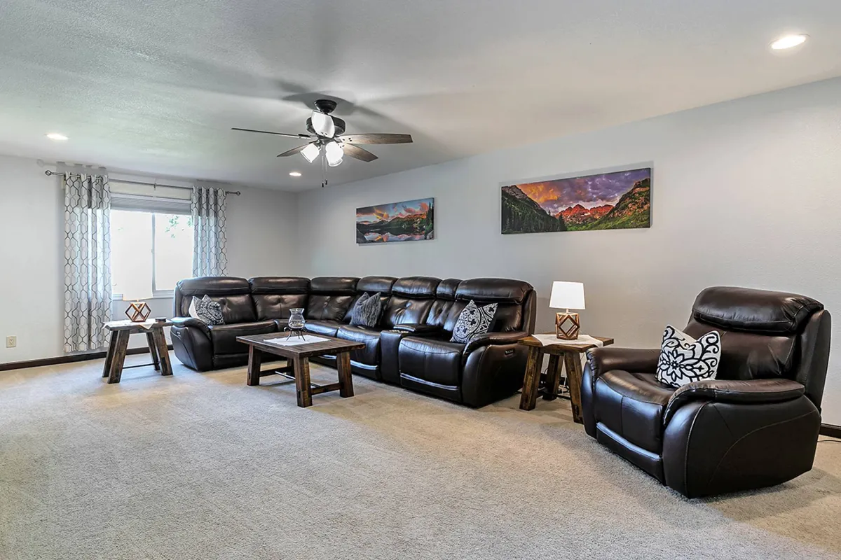 A welcoming living room featuring a large leather sectional sofa, wooden coffee table, tasteful artwork on the walls, and a cozy lamp. The spacious layout is perfect for relaxing, socializing, or watching movies, reflecting the heart of the home.