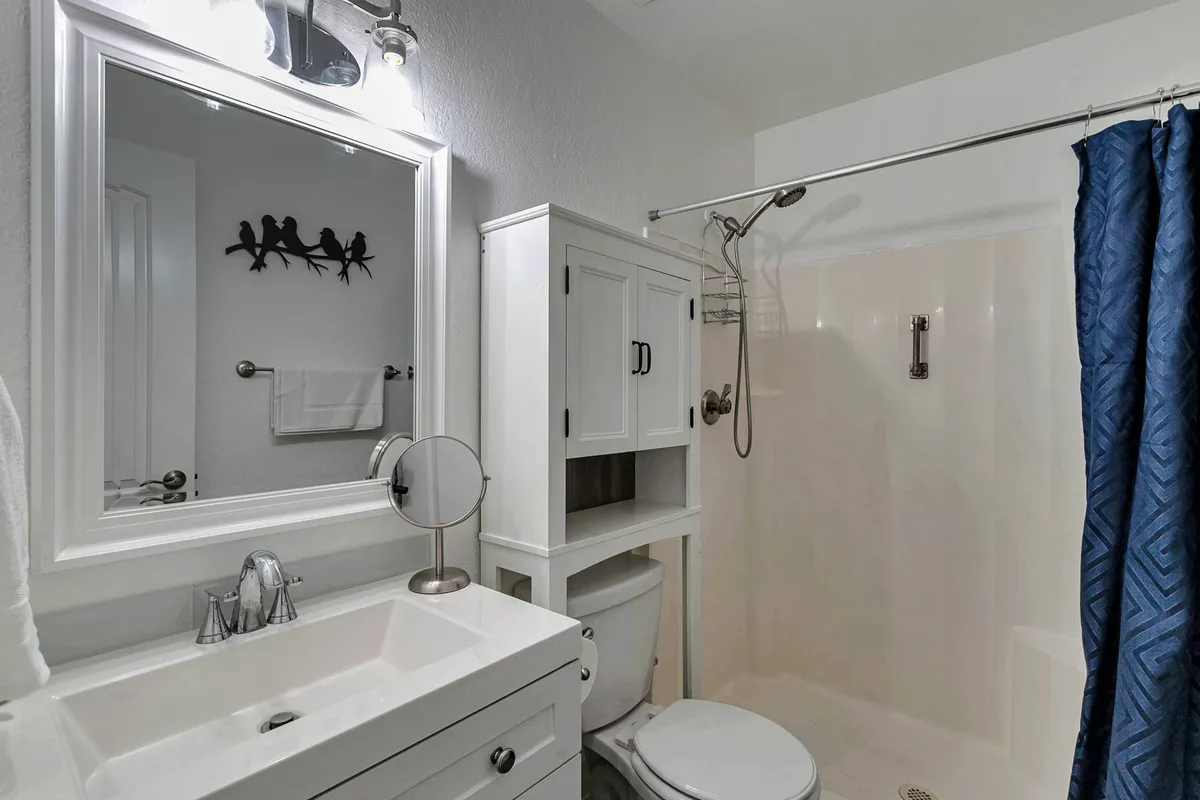 A bright and inviting en suite bathroom with a well-lit vanity, modern mirror, and a blue shower curtain accenting the space. The atmosphere is refreshing, designed for personal relaxation and self-care routines.