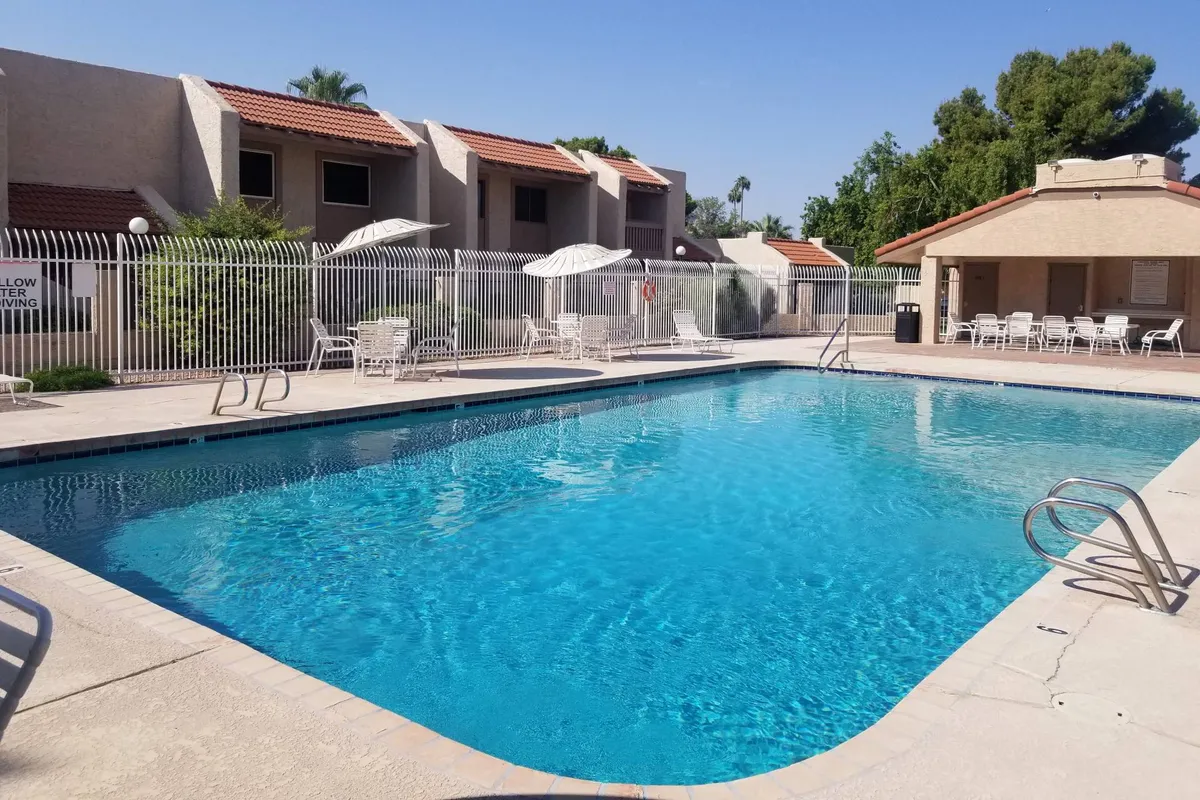 A vibrant exterior view of the sparkling community swimming pool surrounded by several lounge chairs and umbrellas, set amidst lush greenery. The inviting water and poolside seating create a refreshing and social environment ideal for relaxation and sunbathing.