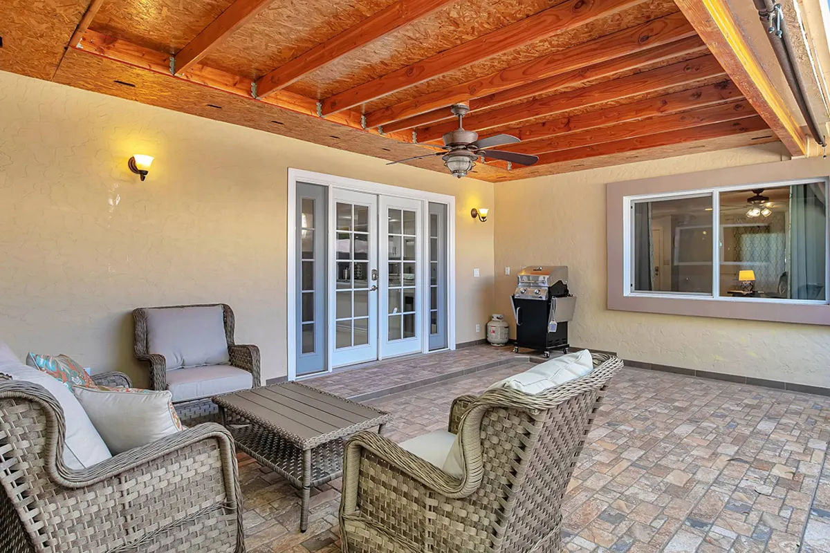 A cozy space with wicker seating, a coffee table, and double French doors opening to a window, offering a glimpse of the private side courtyard. The area is filled with natural light, ideal for quiet moments or casual gatherings.