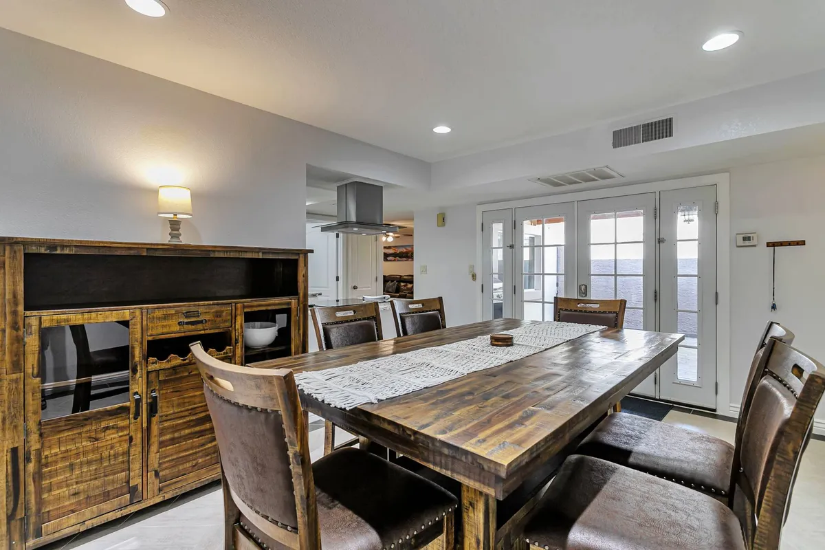 A warm dining space with a dining table, wooden sideboard, and large windows offering ample natural light. The setting exudes a welcoming vibe for group meals or social game nights.