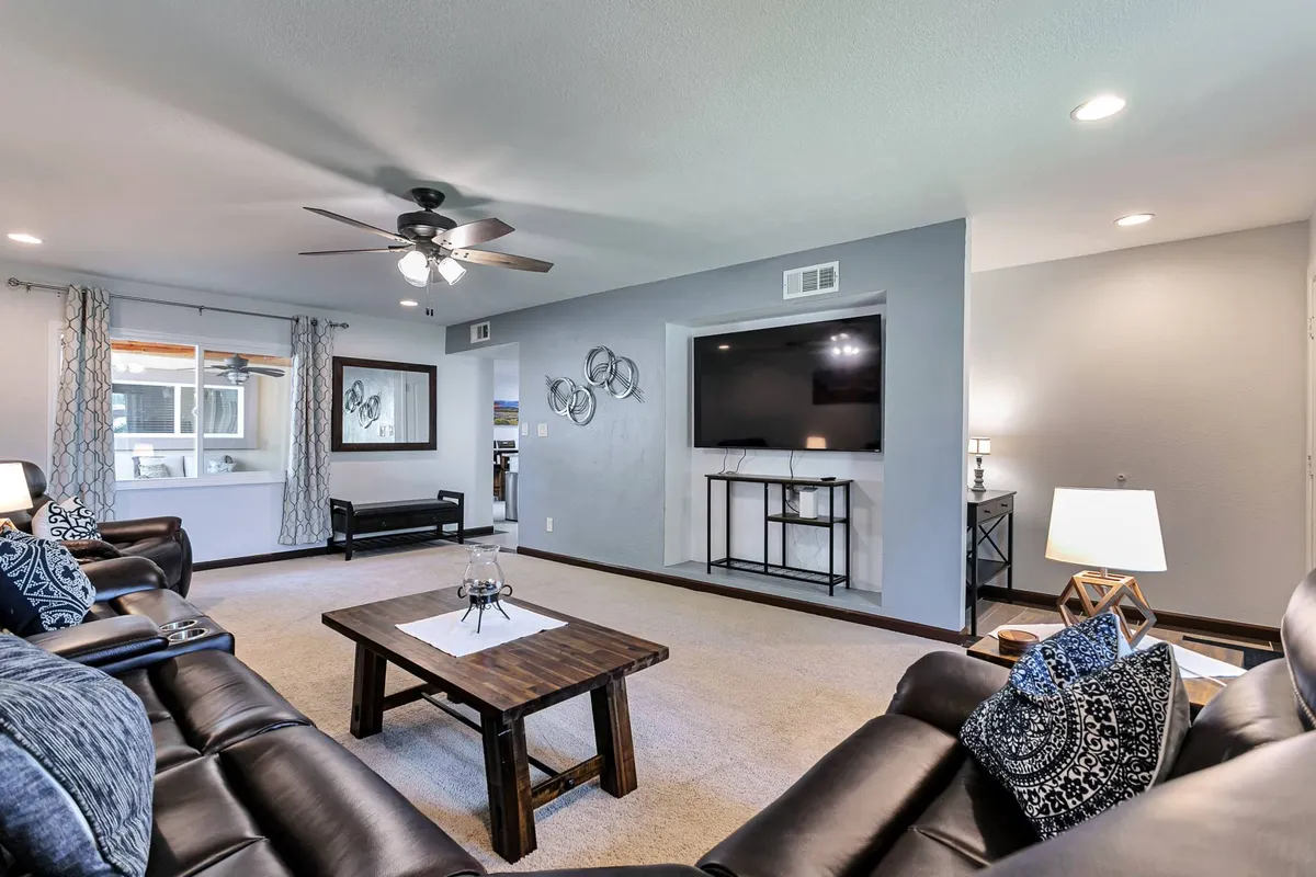 The image showcases a cozy living room with plush leather sofas arranged around a wooden coffee table, facing a wall-mounted TV. Decorative wall art adds warmth to the space, creating an inviting atmosphere perfect for gathering with family or friends.