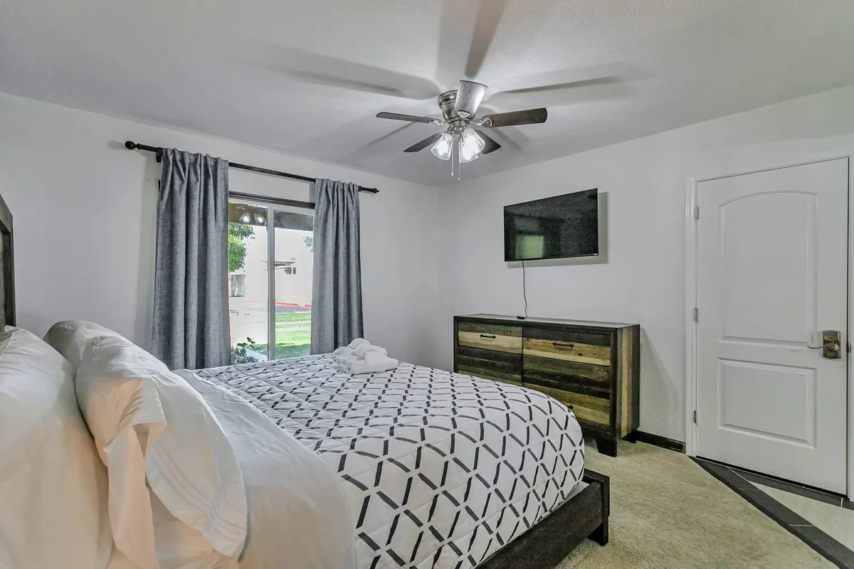 A cozy bedroom setup with a large bed, a window letting in natural light, a dresser, and a television, inviting guests to relax, enjoy quiet moments, or unwind with a movie after a day out.
