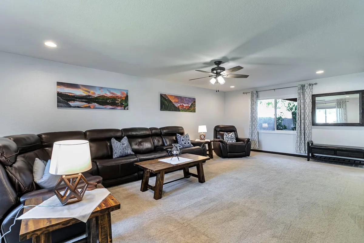 A cozy living room with a leather sofa set, wooden coffee table, decorative wall art, and a large window letting in natural light. The space is designed for relaxation and socializing, reflecting the comforts of home.