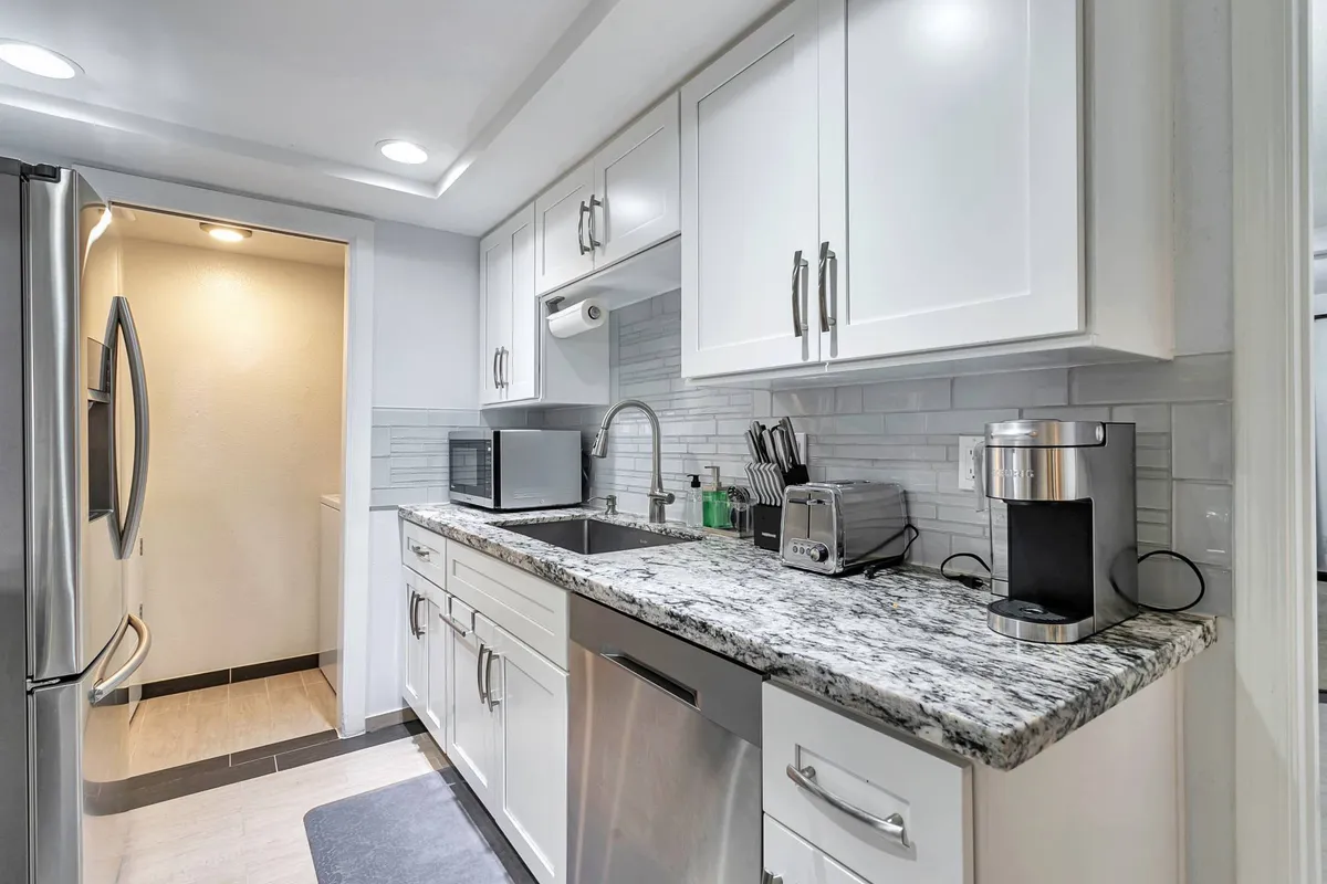 A bright, modern kitchen with granite countertops, stainless steel appliances, and crisp white cabinetry. The layout is both functional and inviting, perfect for preparing meals or gathering with family.