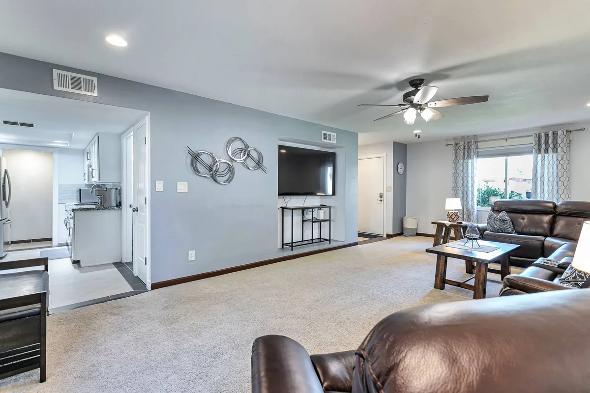 A comfortable living area featuring a leather sofa, coffee table, TV unit with large screen, and decorative wall art. Sunlight filters in through the window, creating a relaxed atmosphere ideal for gatherings.