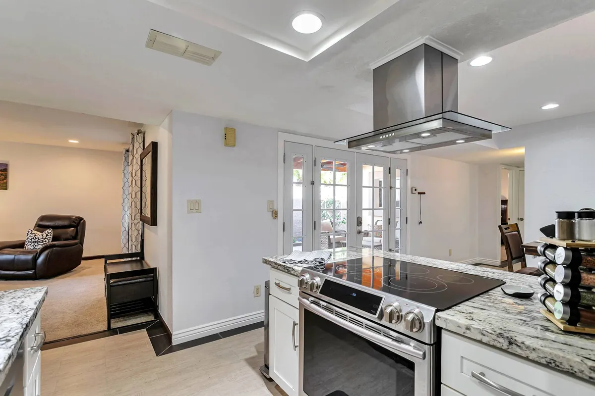 A modern kitchen featuring a sleek kitchen island, stainless steel range hood, granite countertops, and glass sliding doors. The open layout is perfect for cooking, entertaining, and everyday family gatherings.